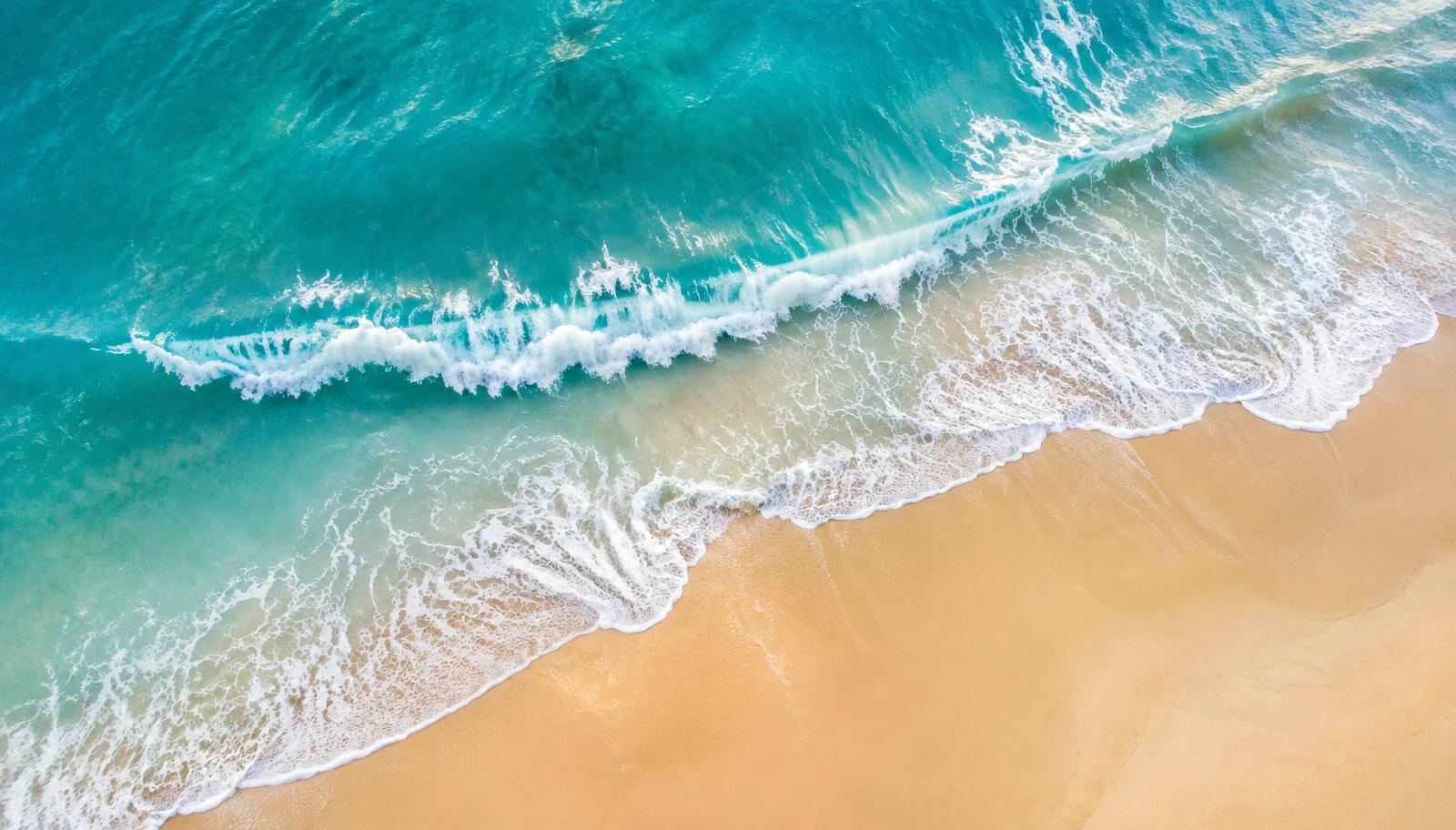Turquoise ocean waves rolling onto a golden sand beach, seen from above